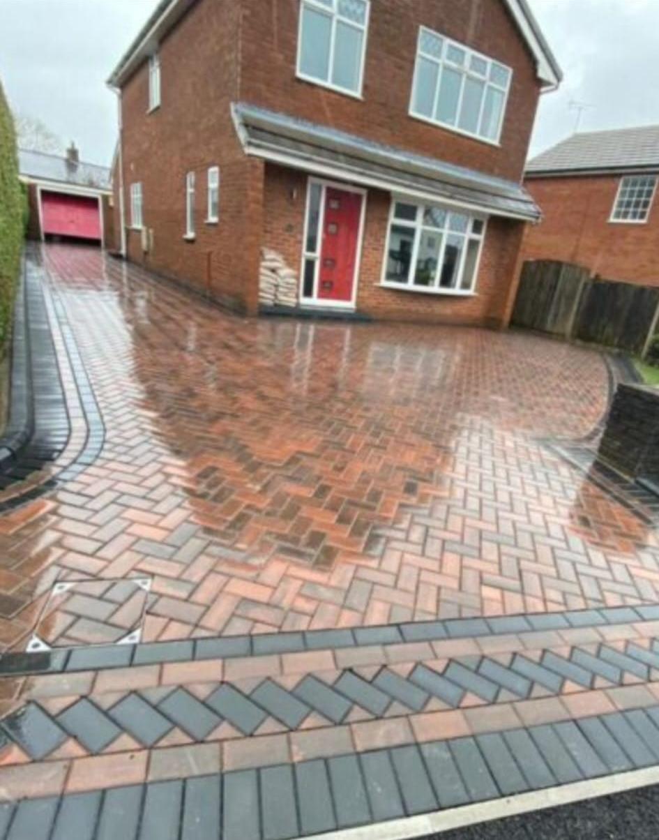 Completed herringbone block paving driveway by LUNA SEN-Scapes in red and brown tones with a double charcoal border, recessed manhole cover and level route to a red-brick house
