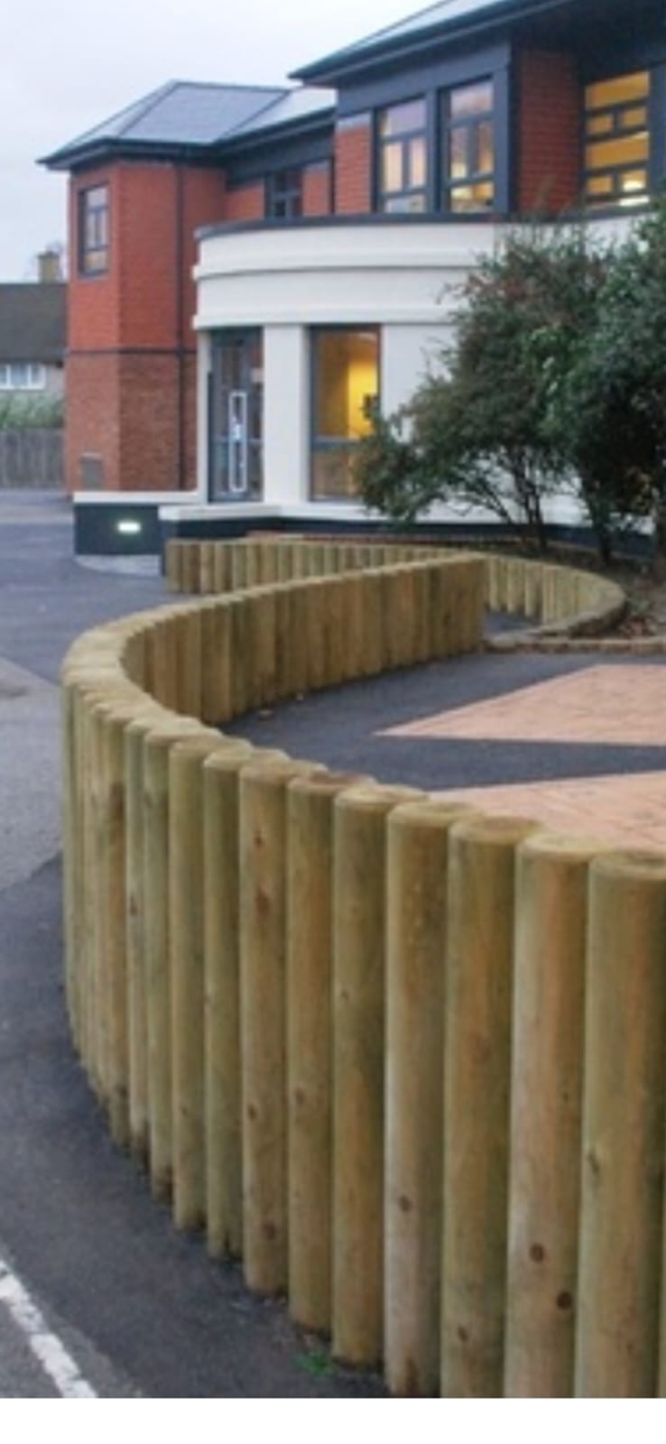 Curved SEN-safe garden boundary of machine-rounded vertical timber posts separating a level asphalt path from planting on a UK family plot by LUNA SEN-Scapes